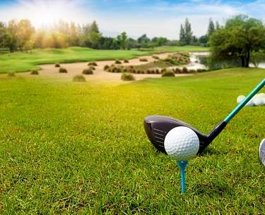 Golf ball on tee ready in green grass on blurred beautiful landscape of golf course with sunrise Golf ball on tee ready in green grass on blurred beautiful landscape of golf course with sunrise