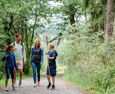 Eine Familie spaziert fröhlich durch einen grünen Wald nahe des Wanderhotels Eine Familie spaziert fröhlich durch einen grünen Wald nahe des Wanderhotels