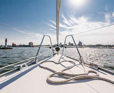 Ein Segelboot fährt im Sommer über ein Gewässer nahe einer Stadt Ein Segelboot fährt im Sommer über ein Gewässer nahe einer Stadt