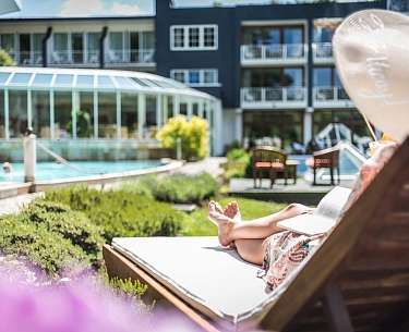 Eine Dame entspannt auf einem Liegestuhl im Außenbereich eines Wellnesshotels Eine Dame entspannt auf einem Liegestuhl im Außenbereich eines Wellnesshotels