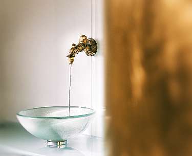 Aus einem goldenen Wasserhahn läuft Wasser in ein gläsernes Waschbecken Aus einem goldenen Wasserhahn läuft Wasser in ein gläsernes Waschbecken