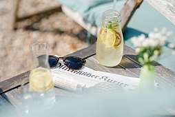 RH Reichshof Blick auf einen Tisch mit Sonnenbrille, Zeitung und sommerlicher Limonade