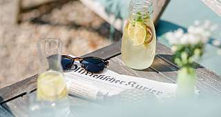 Blick auf einen Tisch mit Sonnenbrille, Zeitung und sommerlicher Limonade