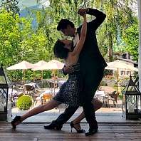 Tangowoche Ein Pärchen tanzt vor Baum- und Bergkulisse auf einer Veranda Tango