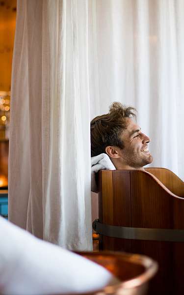 Ein Hotelgast liegt in einer hölzernen Badewanne in einem exklusiven Wellnesshotel Ein Hotelgast liegt in einer hölzernen Badewanne in einem exklusiven Wellnesshotel