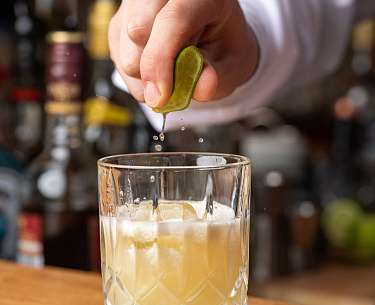 Bar Eine Limette wird über einem Cocktail ausgepresst