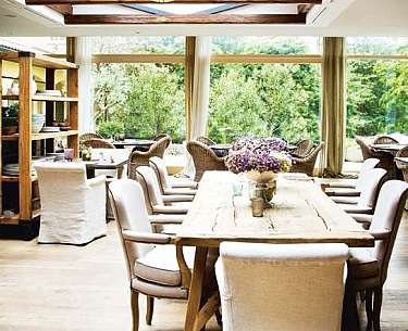 Bright dining room with a long wooden table, upholstered chairs and large windows overlooking the garden.
