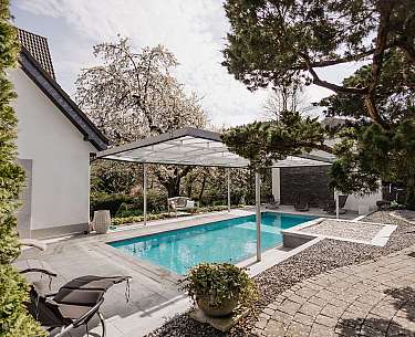 Blick auf einen modernen Pool mit Gartenstühlen und begrüntem Garten