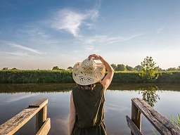 RH Reichshof Frau mit Hut von hinten blickt auf einen See