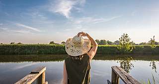 Frau mit Hut von hinten blickt auf einen See