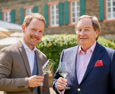 Familie Brennfleck Blick auf den Vater und Sohn der Familie Brennfleck, die jeweils ein Glas Weißwein hochheben