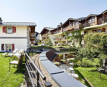 View of an alpine hotel with balconies, garden and outdoor terrace in sunshine.