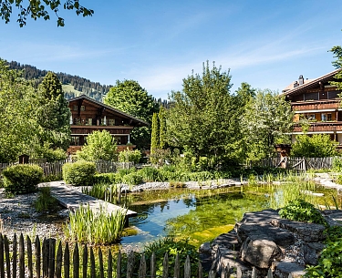 Schwimmteich im Hotel Garten Schwimmteich mit Steg vor dem traditionellen Hotelgebäude