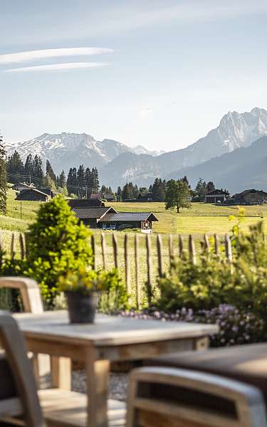 Sitzbereich auf Terrasse mit Blick auf grüne Wiesen und schneebedeckte Berge im Hintergrund