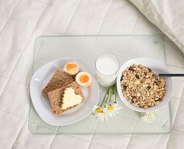 Frühstück im Bett Müsli, Eier und Brot auf einer Platte im Bett
